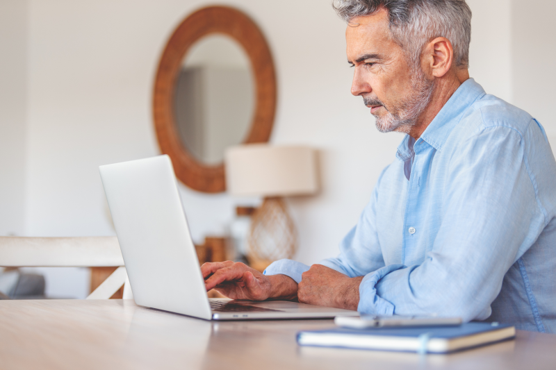 Mature businessman working on a laptop at home. He looks a little worried and stressed and casually dressed.